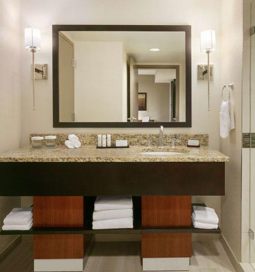 A granite countertop with sink rests on a wooden vanity with a mirror above with wall lights on either side, highlighting the need for regular bathroom vanity repairs to stay up-to-date