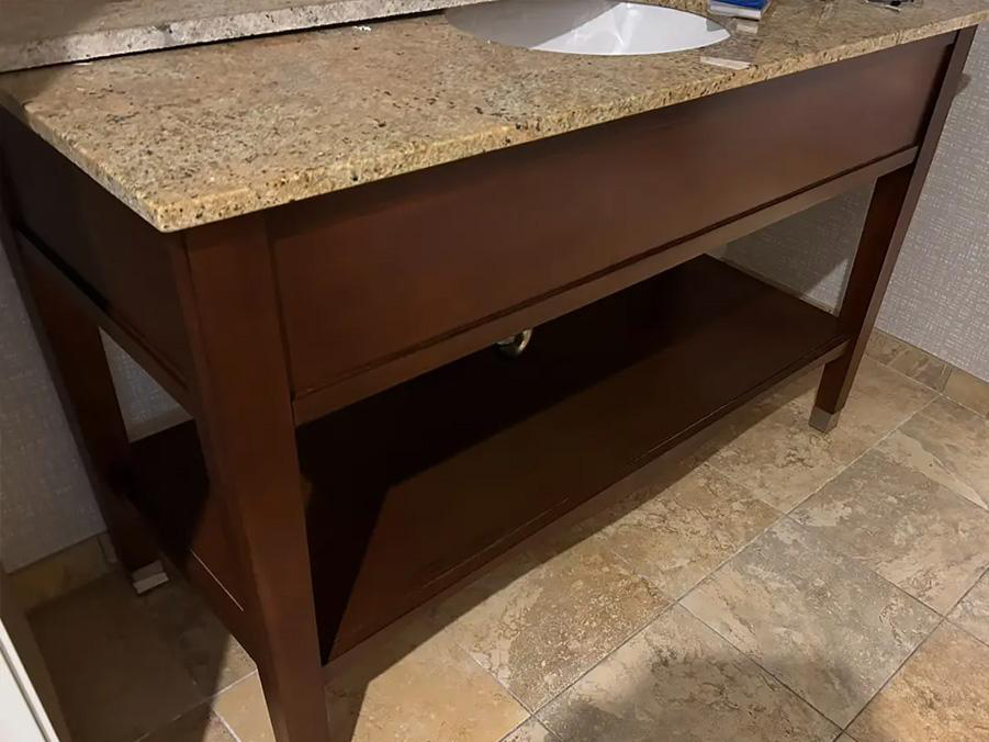 A wooden vanity with a granite countertop on a tiled floor shows the difference bathroom vanity repairs can make in the appearance of the bathroom fixtures